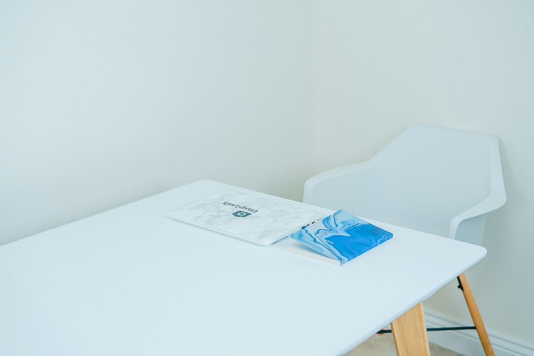 Bright, modern, and welcoming therapist's office with a laptop open on a clean desk next to a green plant, signifying the ...