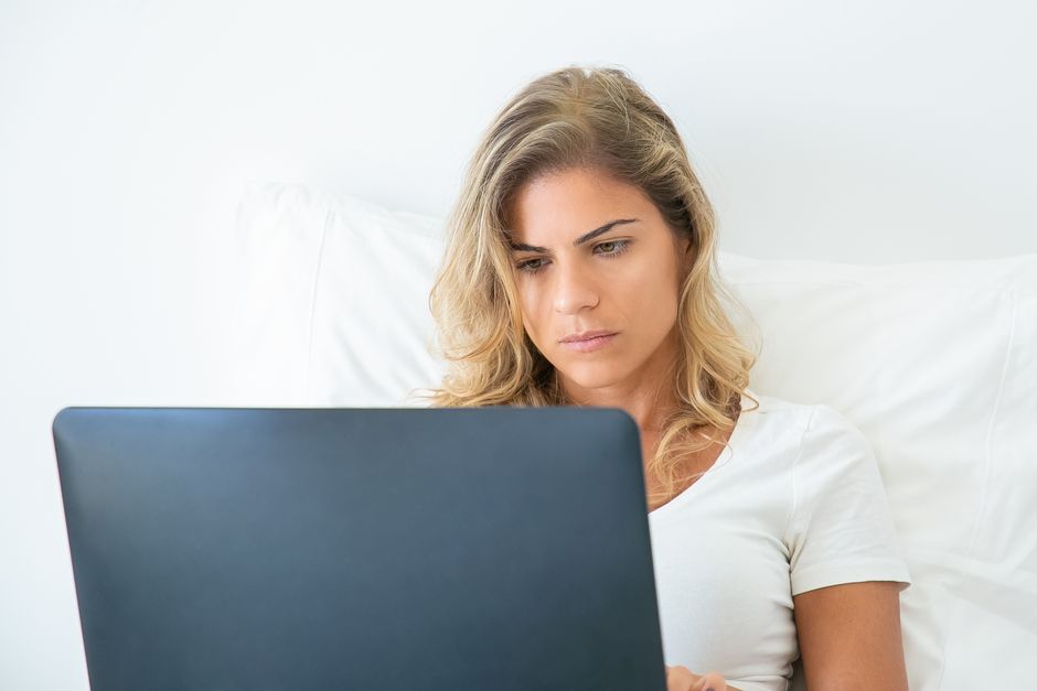 A professional and friendly therapist sits in a calm, sunlit office, thoughtfully working on a laptop, representing the management of a modern therapy practice.